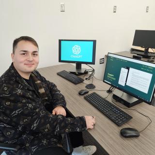 Andrew Szilagyi sitting in front of a computer and smiling at the camera. ChatGPT is on the screen in the background.