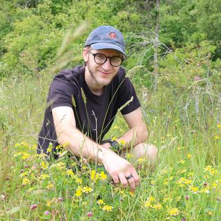 Bryan Lamprecht kneels in front of a patch of Hosackia pinnata flowers nestled in a field of grass.