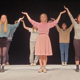 Six actors stand in two lines holding their arms up over their heads while rehearsing a scene at Malaspina Theatre.