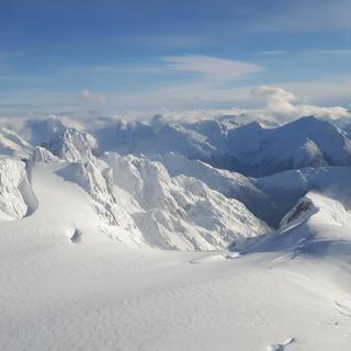 Mountain peaks covered in snow with a cloudy blue sky overhead.