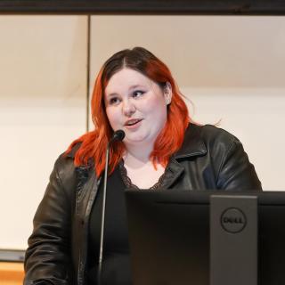 A student stands in front of a microphone in a classroom.