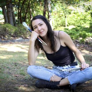 Kashmir Lesnick-Petrovicz sits on the ground and holds paint brushes in her hands.