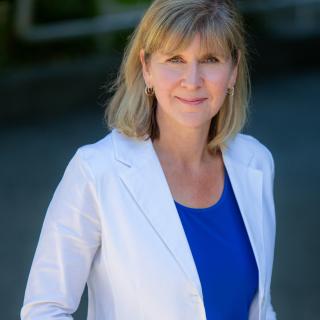 Kristie Dewald with a blurred background, wearing a white blazer