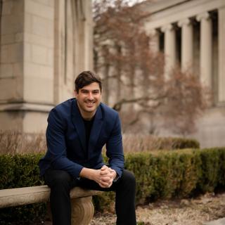 Michael MacKenzie sits on a bench in front of a stone building