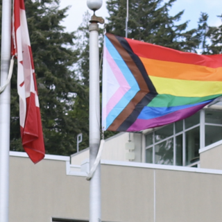 Two flagpoles side by side. One holds the Canada flag and the other the Pride flag.