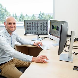 Sandy sits at his desk with images of brains open on one screen