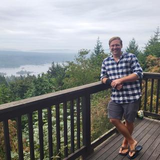 Stephen Hextall leans against a railing with trees and a lake in the background.