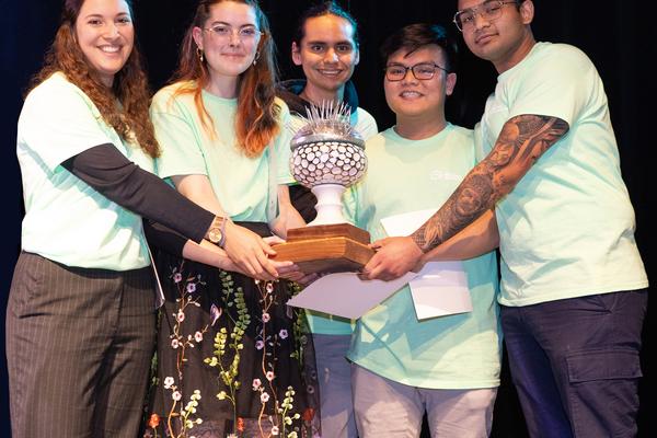 A group of students holds a trophy, all are wearing green shirts