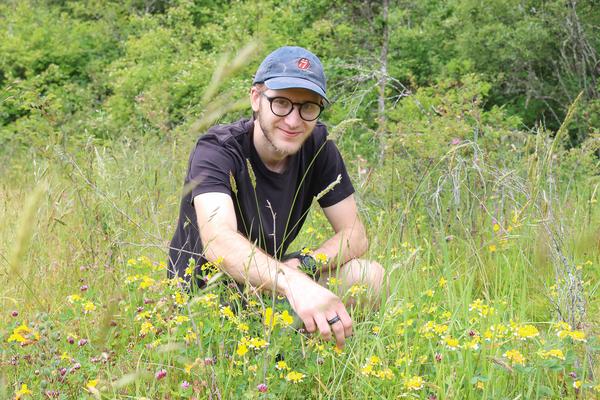 Bryan Lamprecht kneels in front of a patch of Hosackia pinnata flowers nestled in a field of grass.