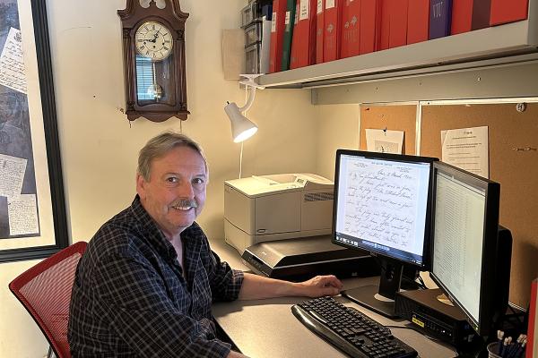 Stephen Davies sits at his computer with a digitized letter on the screen