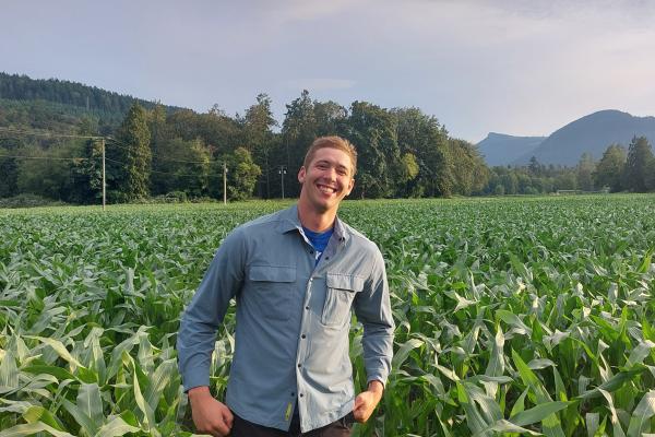 Douglas Groenendijk grins while standing in a vast green field with a mountain range behind him.