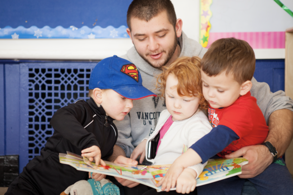 An early childhood educator reading a book to three kids