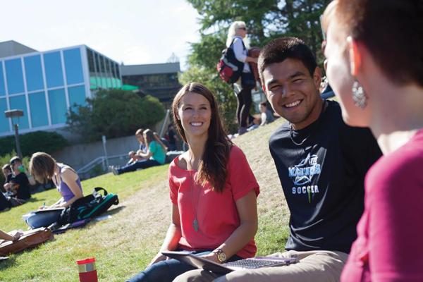 Three students sitting on lawn interacting with each other