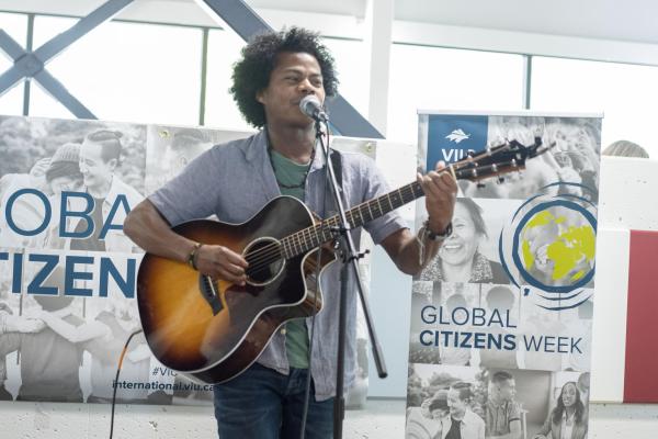 Student sings and plays guitar with Global Citizens Week banners behind him