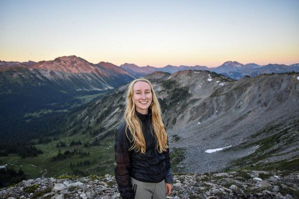 Kelsey Moore smiles with a mountain range at sunset behind her.