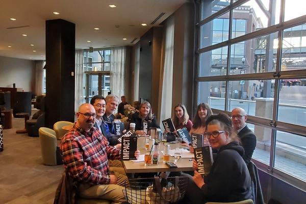 A group of people sit at a table, all holding copies of the same book