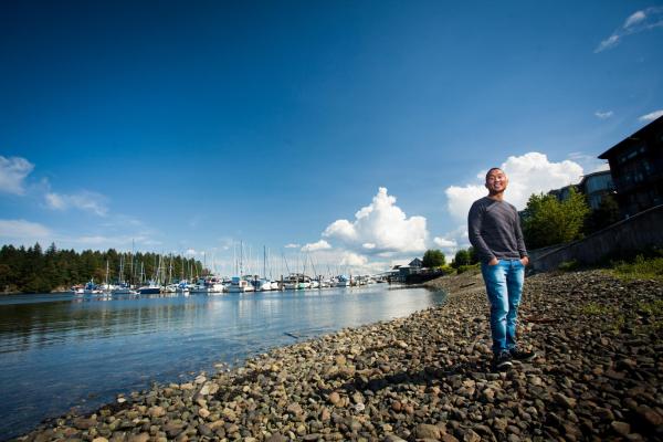 A man stands in the foreground with the waterfront and a marina full of boats behind him