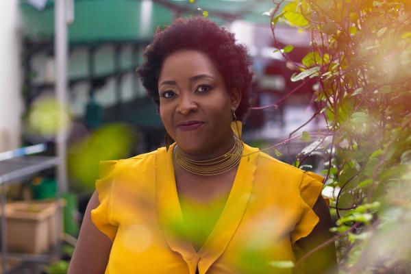 Ozoz Sokoh, wearing a bright yellow shirt, stands in a garden area.