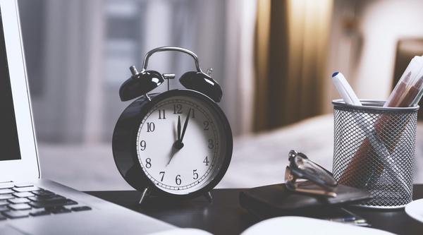 A clock on a desk next to a laptop and pen holder