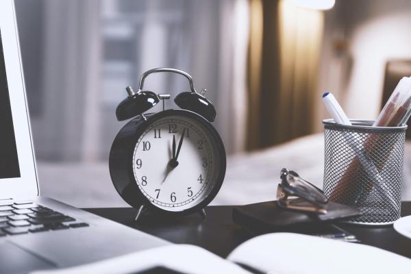 A clock on a desk next to a laptop and pen holder