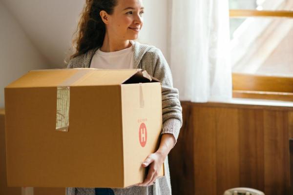 A girl holds a moving box while standing in a bedroom