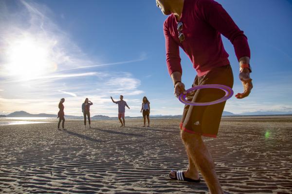 Students play frisbee at a beach