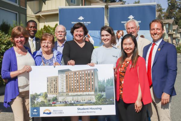 Group photo of people standing with a rendering of the new student housing building