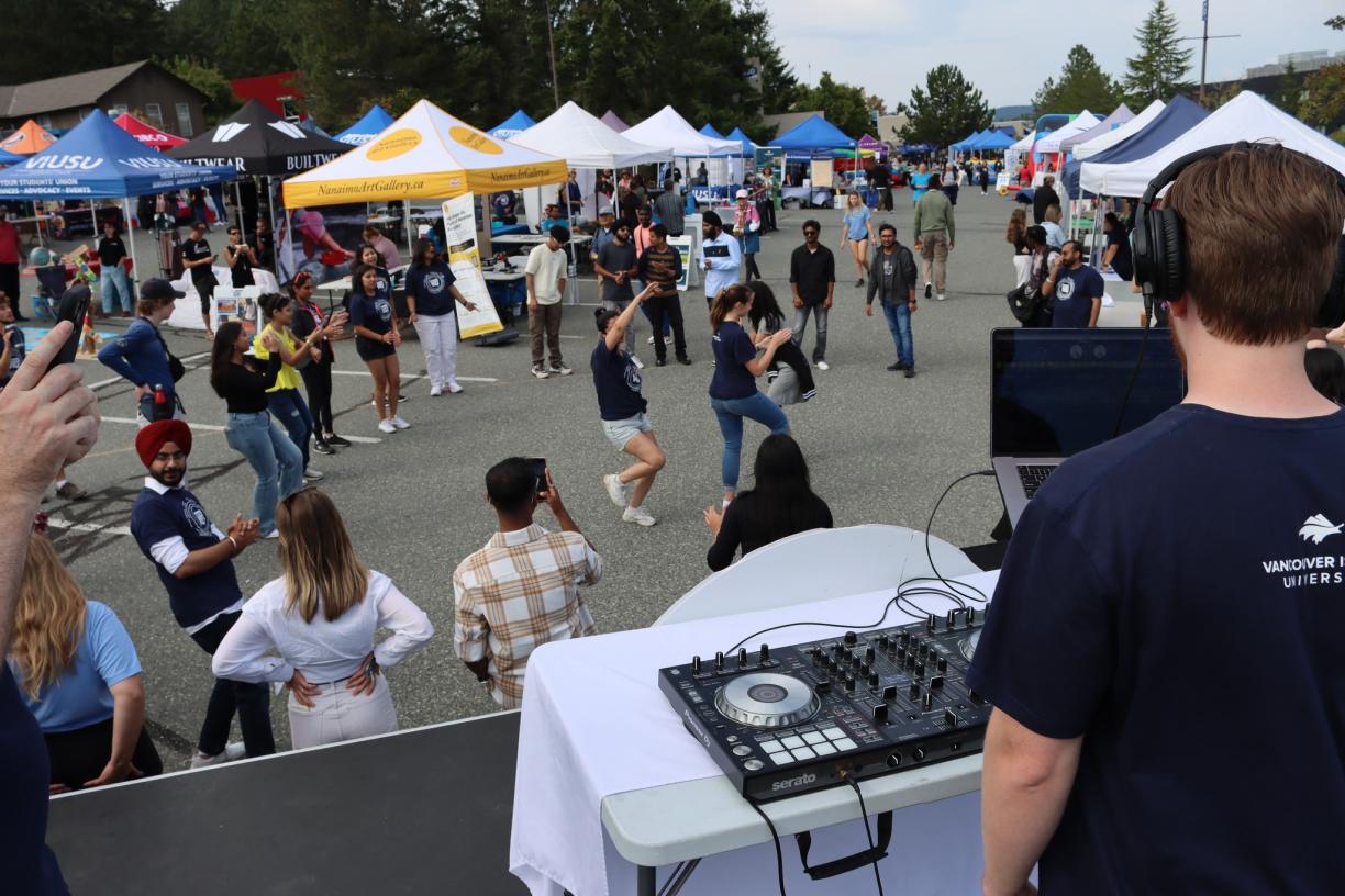 A DJ on a stage plays music while people dance in the background