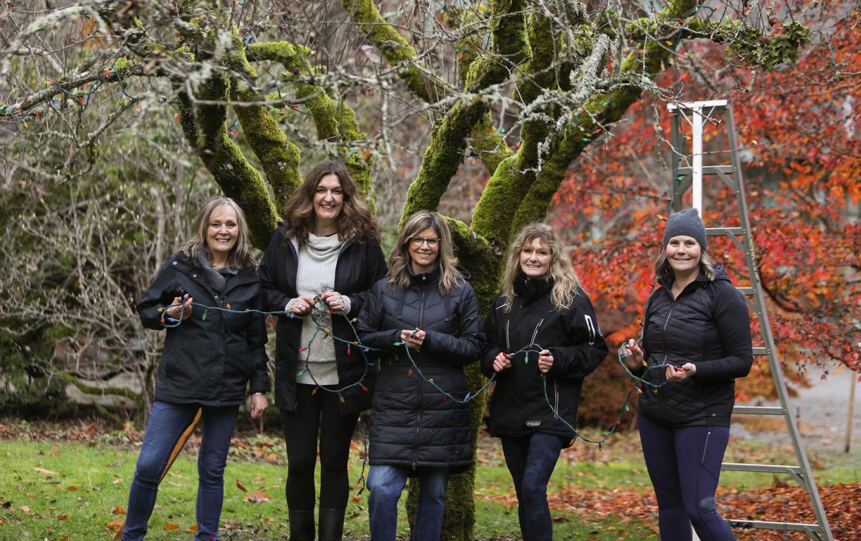 Five people stand with Christmas lights in their hands.