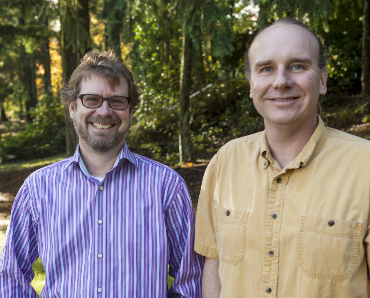 Dr. Erik Krogn and Dr. Chris Gill stand beside each other in a wooded area