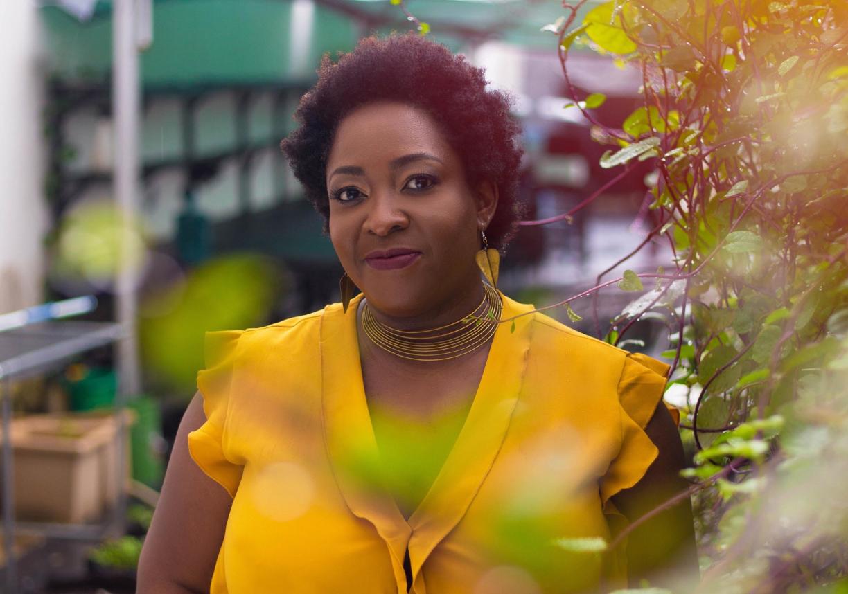 Ozoz Sokoh, wearing a bright yellow shirt, stands in a garden area.