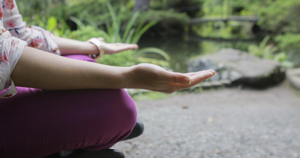 A woman meditates on a wooden bench next to a koi pond at Vancouver Island University