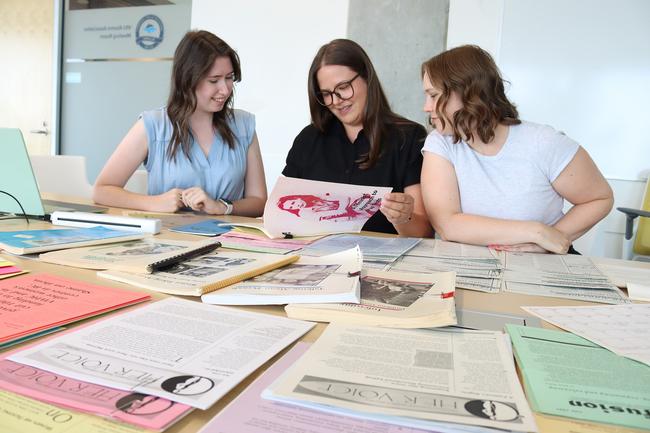 VIU Research Assistant Elise Cullon, Dr. Whitney Wood and Katie Carroll look at historical documents laid out on a desk.